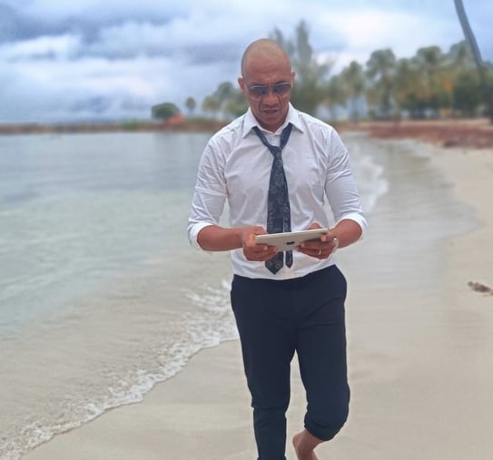 « Bruno Valery en réflexion stratégique, tablette en main, marchant sur une plage paradisiaque en Guadeloupe »