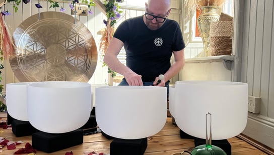 a man sitting on a wooden floor with crystal signing bowls