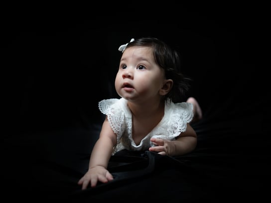 a baby girl in a white dress and a black background