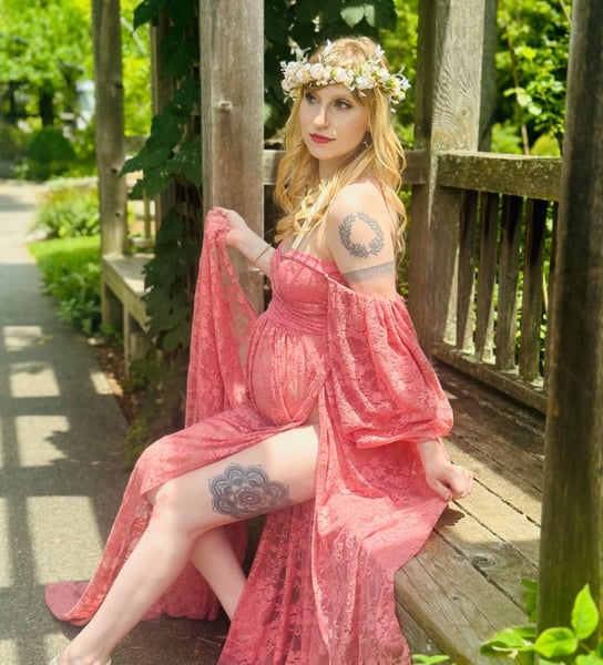 Pregnant woman in a crown and pink gown sitting on a wooden bench during maternity photoshoot—celebrating motherhood.