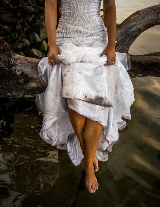 Robe de mariée sale et mouillée Trash The Dress sur une branche au bord de l'eau