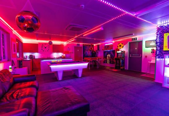 a bright neon-lit room with a pool table and games area and sensory room