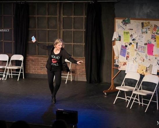 a woman Amy Cave in a black top tap dancing on stage in a play.