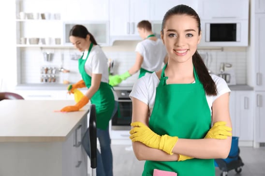 a woman in green aprons and gloves holding a cleaning sponge
