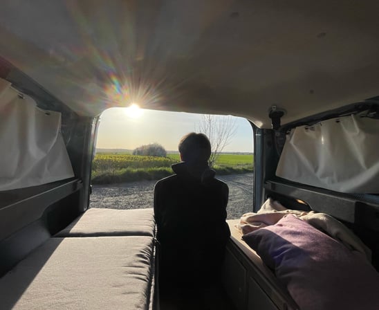 Person sitzt entspannt im selbst ausgebauten Dacia Dokker Camper, mit geöffneter Hecktür und Blick i