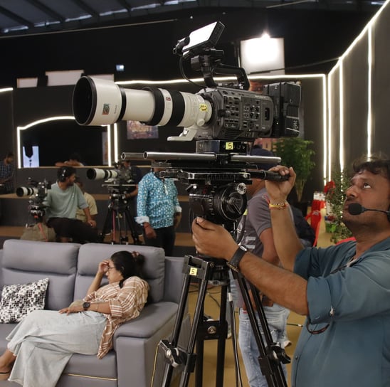 a man is filming a video camera and a woman is sitting on a couch