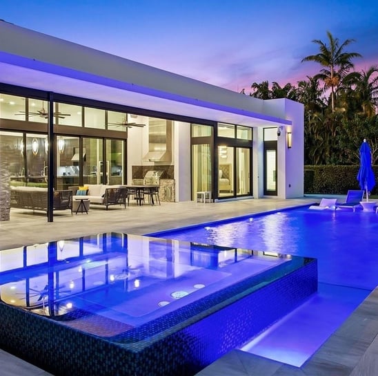 a fiberglass pool in a backyard with blue lights and a spa with infinity edge to the swimming pool