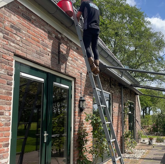 Man op ladder die dakgoot leegmaakt tijdens dakgootreiniging in Groningen