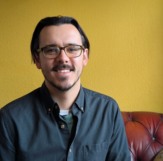 Tom King smiling towards the camera, with a yellow background.
