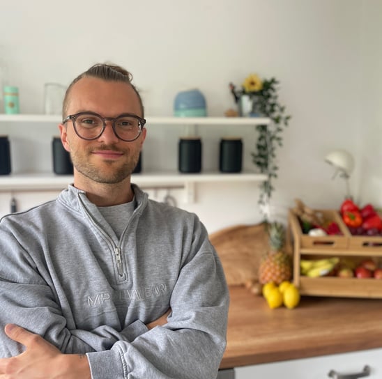 ein mann mit Brille und bart, der lächelnd in einer Küche steht vor Obst und Gemüse