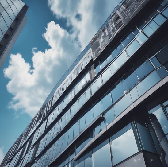 A modern office building with a geometric, pyramid-shaped top. The architecture features reflective glass windows and a beige stone exterior. The name 'Mutua Madrileña' is displayed near the top.
