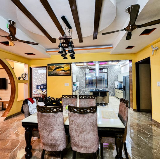 A stylish dining area with wooden beams, decorative lighting, and an open kitchen layout.