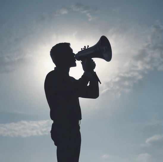 A silhouette of a person holding a megaphone against a clear blue sky, suggesting communication or a call to action.