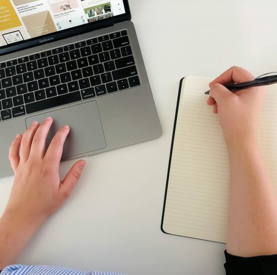 a person's hand is holding a pen and writing on a notebook