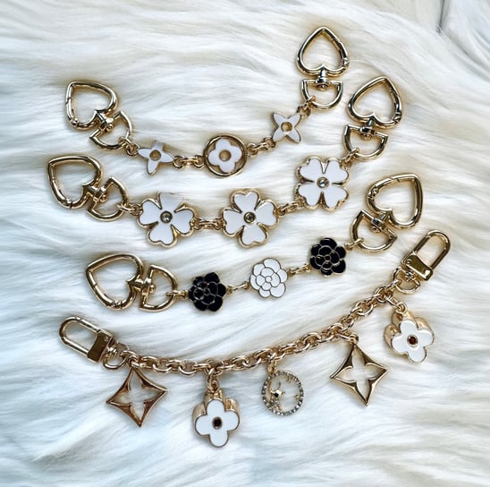 Gold-toned chain accessories featuring heart-shaped links and enamel flower charms in white and blac