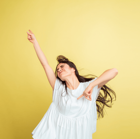L'immagine mostra una donna che indossa una blusa bianca, posando con un'espressione energica e gioiosa su uno sfondo giallo.