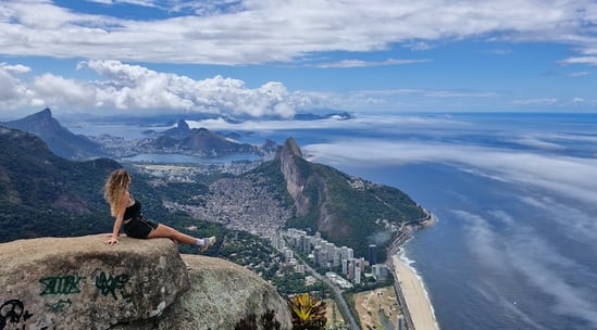 imagem com uma mulher sentada na beira da pedra da Gávea no Rio Janeiro