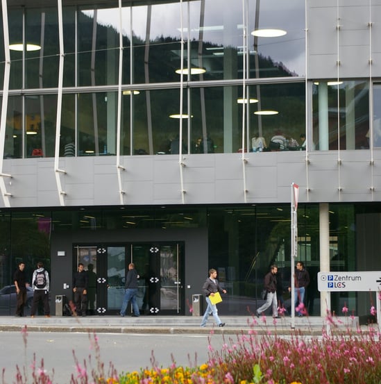 Auf dem Bild ist der Neubau der Montanuniversität Leoben zu sehen. Menschen benutzen den Gehweg.