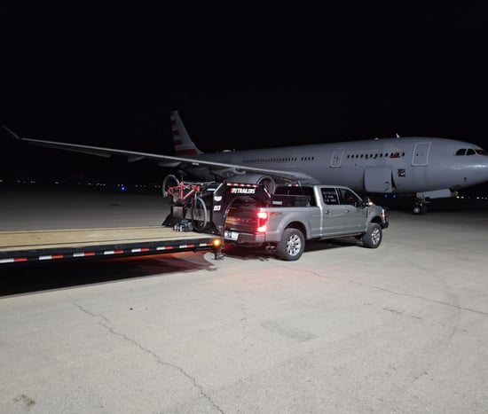 a truck with a flatbed and a flatbed trailer parked in front of a plane