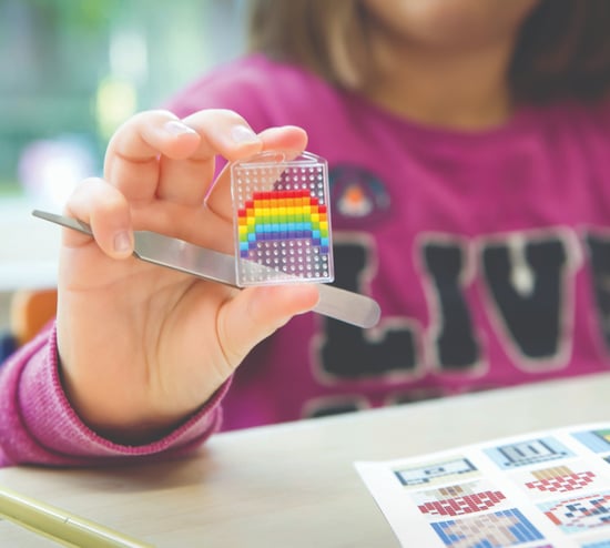 Mergaitė rodo spalvingą vaivorykštės paveikslėlį ant skaidraus pagrindo, kurį ji sukūrė iš pikselių