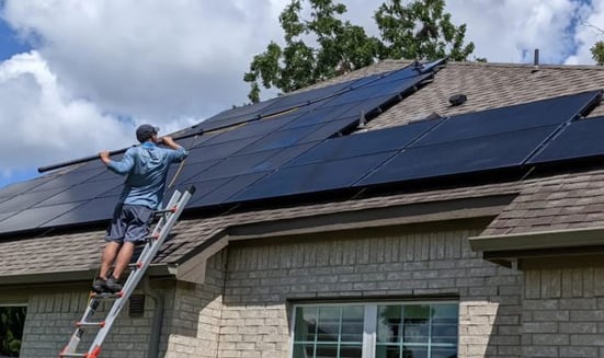 A man standing from a ladder cleaning solar panels on a roof with a water pool