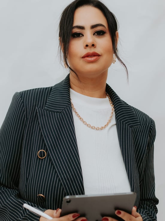 a woman in a suit and necklaces holding a tablet