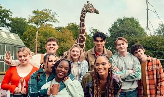 The Heartstopper ensemble cast posing in front of giraffe during season 3 filming.