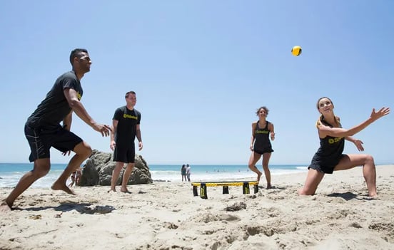 deux équipe de deux personnes s'affrontent au spikeball sur la plage