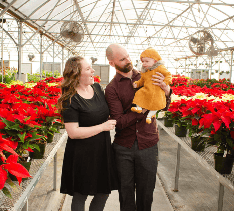 a man and woman holding a baby in a greenhouse