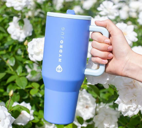 a person holding a blue coffee mug in front of a bush