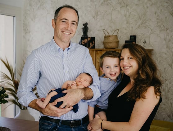 Photo de famille à domicile avec maman, papa, bébé et grand frère souriants – séance naissance Gard