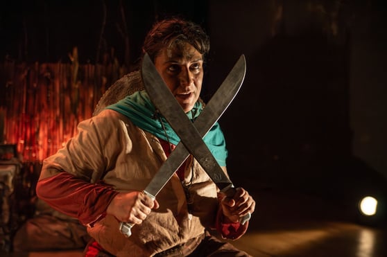 a man in a brown jacket holding two large knives