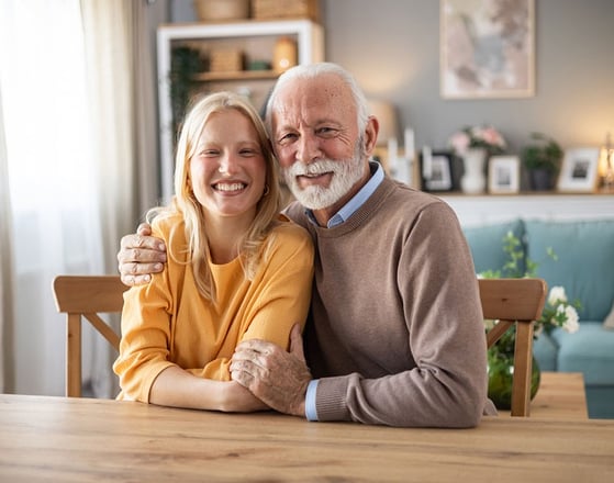 A grandparent sitting at the table hugging his autistic young adult granddaughter