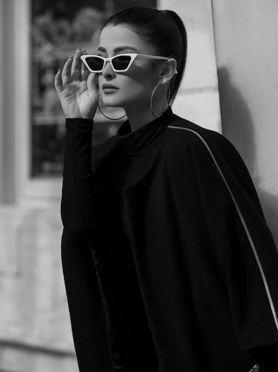 A stylish brunette woman with hoop earrings in all black wearing holding her white sunglasses with her right hand