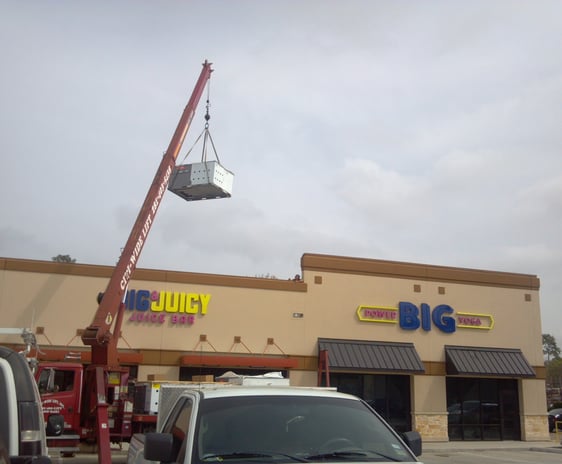 a crane is lifting a commercial A/C unit to roof