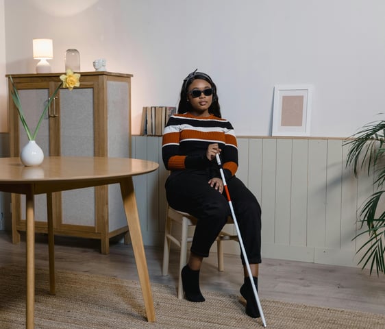 Blind woman with walking stick sitting in a chair beside a dining room table