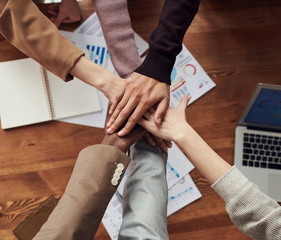 Diverse group of professionals joining hands in a teamwork gesture, symbolizing collaboration,