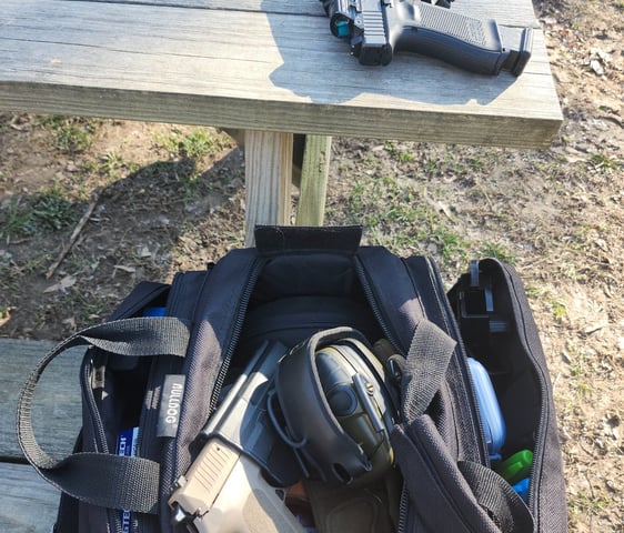Black bag with ear protection and 2 self-defense firearms one with red dot one without.