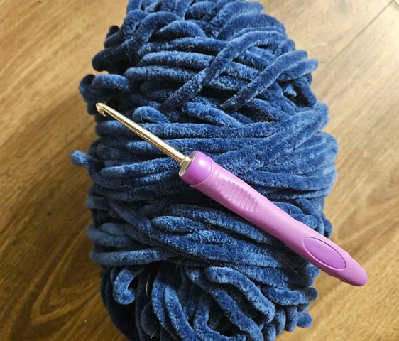 Une pelote de laine bleu avec un crochet violet