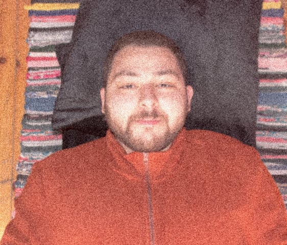 Amr El Khelawy. A man wearing a brick red jacket. Lying on the floor. Looking to the camera. Smiling