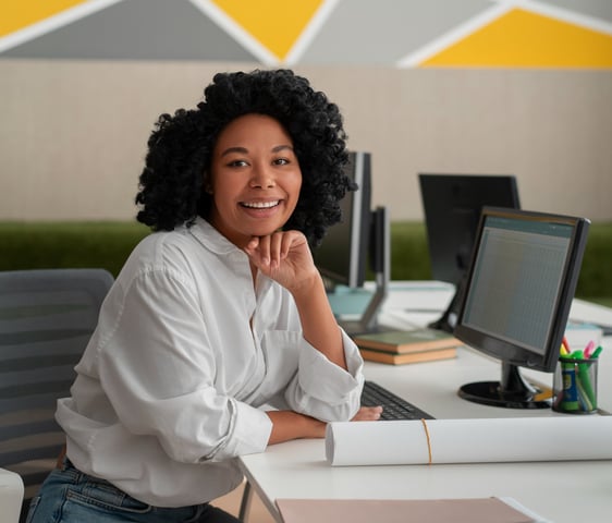 a woman sitting at a desk with a laptop and a computer