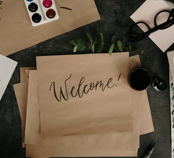 Handwritten welcome card surrounded by creative tools, symbolizing an open invitation...