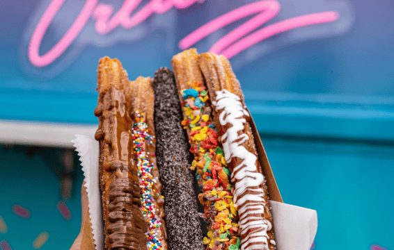 a person holding a box of donuts with chocolate and sprinkles