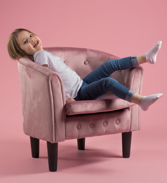 Enfant sur un fauteuil rose qui rit et lève les pieds, sur fond rose