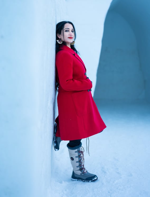a woman in a red coat and boots standing in the snow and leaning on snow wall