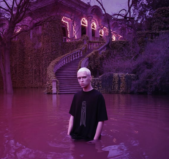 man model wearing Fulutee black T-shirt with Fu talisman Love Magnet design, standing in pink water