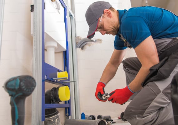 man hunched over, installing plumbing