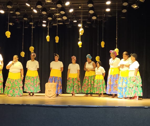 Ciganinhas se apresentam em palco com saias coloridas, turbantes e iluminação cênica
