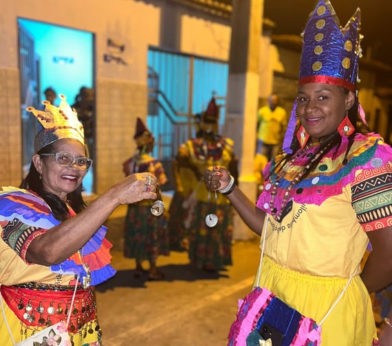Ciganinhas sorrindo e dançando à noite com trajes coloridos e coroas em celebração quilombola