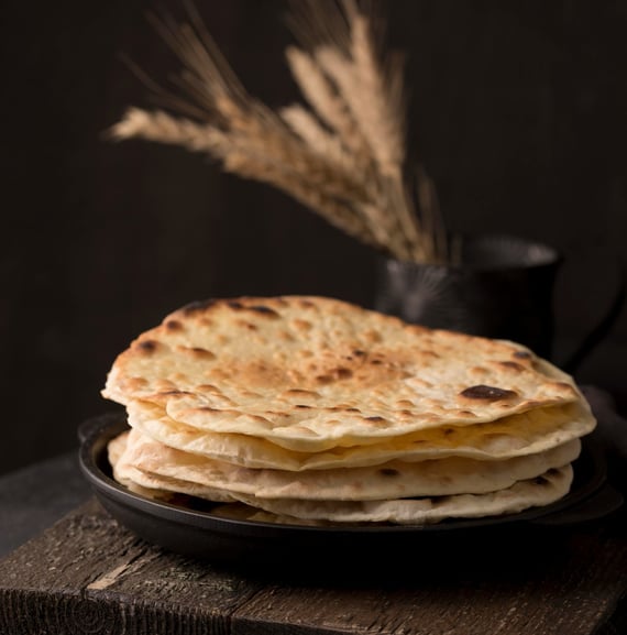Pão sírio caseiro, fresquinho e macio, com textura levemente dourada, disposto em uma tábua rústica.